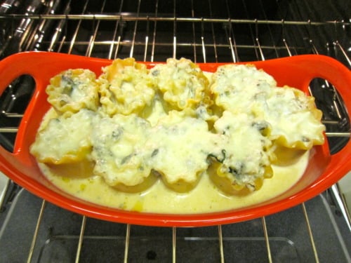Spinach and mushroom lasagna roll-ups topped with creamy Gorgonzola sauce, baking in a red dish in the oven.