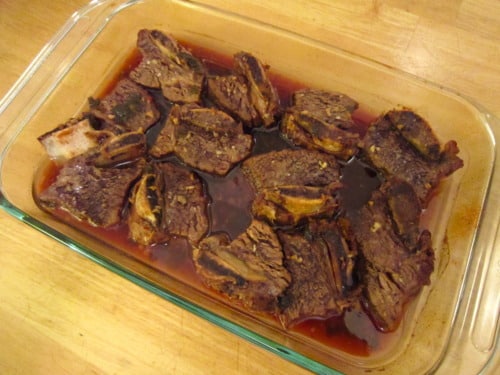 Braised beef short ribs in a glass baking dish with rich cooking liquid.