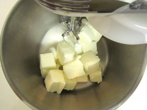 Cream cheese cubes and sugar in a mixing bowl before blending.