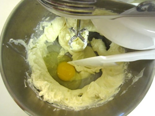 Creamed cheesecake mixture in a mixing bowl with an egg added, ready to blend.