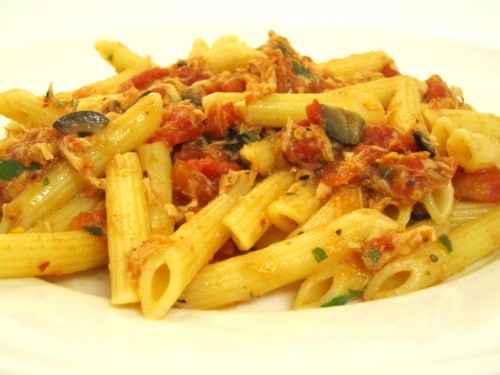 Plate of penne pasta tossed with tuna, tomatoes, olives, parsley and chili flakes in a puttanesca-style sauce.