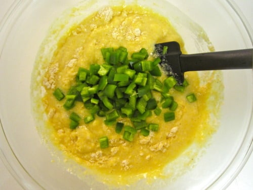 Cornbread batter in a mixing bowl with chopped jalapeños and a black spatula.