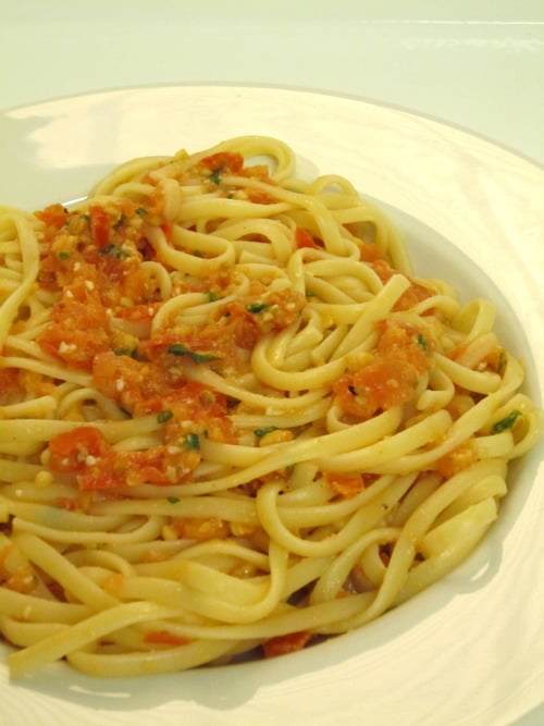 Linguini pasta served with a chunky tomato-based sauce, garnished with herbs on a white plate.