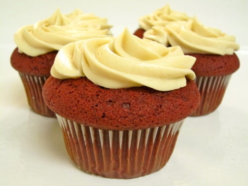 Red velvet cupcakes topped with vanilla cream cheese frosting on a white surface.