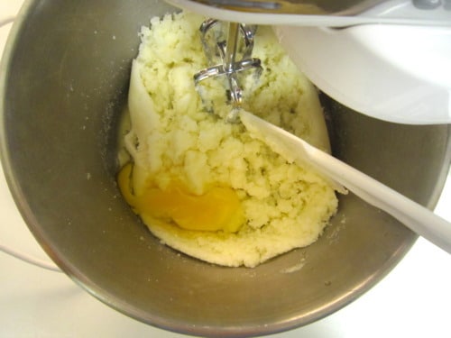 Egg added to creamed butter and sugar in a mixing bowl with a hand mixer.