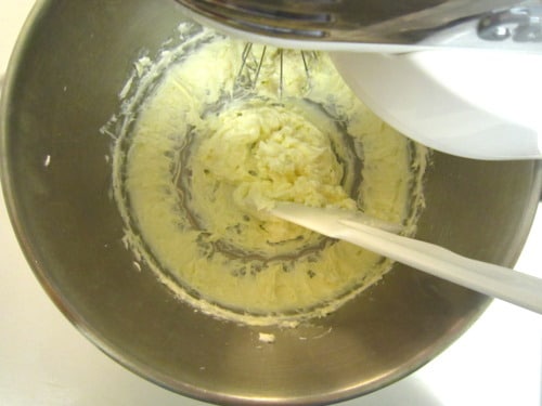 Vanilla cream cheese frosting being mixed in a metal stand mixer bowl with a spatula, viewed from above.