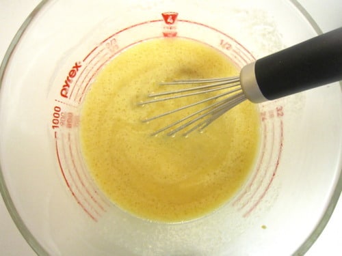 Wet ingredients including eggs and sugar being whisked together in a glass measuring cup, prepared for apple fritter muffins.