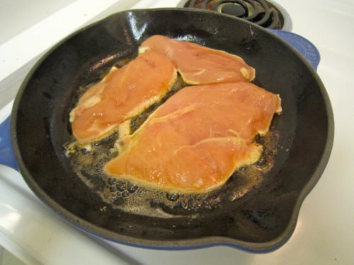 Chicken breasts cooking in a cast iron skillet with bacon fat, prepared for bacon fat chicken alfredo.