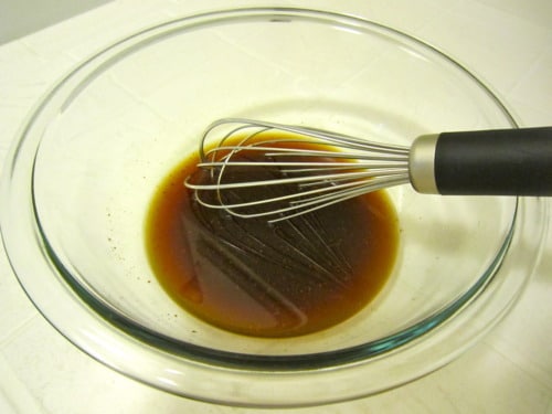 Whisk mixing brown sauce in a glass bowl for Thai chicken with rice noodles.