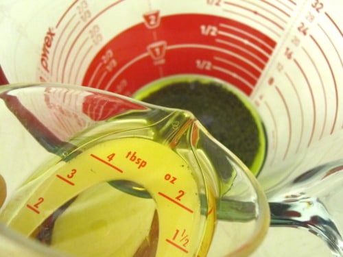 Olive oil being poured into a measuring cup with poppy seed vinaigrette for strawberry spinach salad.