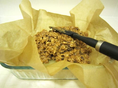 Granola bar mixture with oats and almond butter pressed into a parchment-lined baking dish.