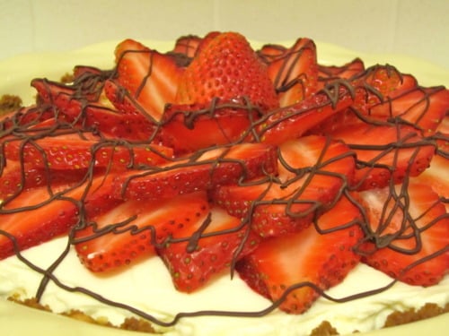 Strawberries and cream pie topped with sliced fresh strawberries and drizzled with chocolate on a graham cracker crust.