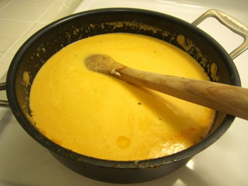 Creamy buffalo cheese sauce being stirred with a wooden spoon in a saucepan for buffalo chicken macaroni and cheese.