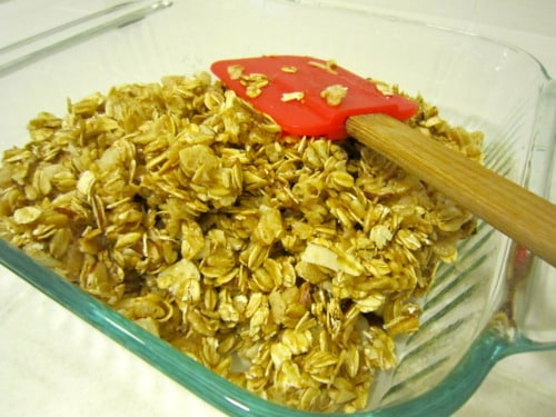 Oat mixture for no-bake chewy chocolate chip granola bars in a glass baking dish with a red spatula.