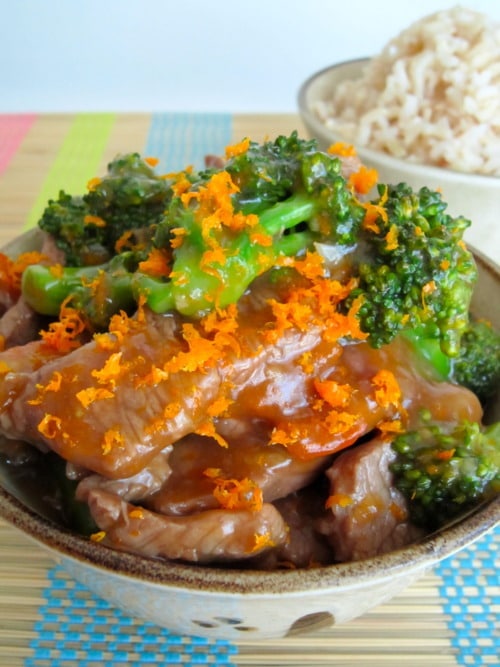Bowl of orange beef and broccoli topped with fresh orange zest, served with a side of brown rice.