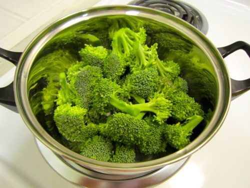 Fresh broccoli florets steaming in a pot on a stovetop.
