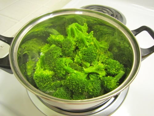 Steamed broccoli florets in a stainless steel pot on a stovetop.