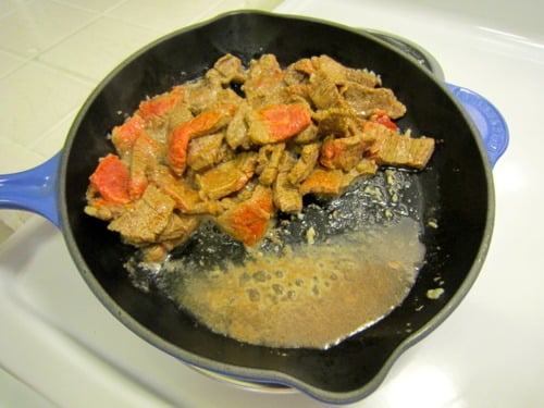 Sliced beef searing in a skillet with orange zest and sauce as part of orange beef and broccoli preparation.