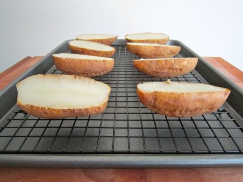 Halved baked potatoes placed on a wire rack over a baking sheet, prepared for making loaded potato skins.