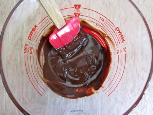 Melted chocolate brownie cookie batter being stirred with a red spatula in a glass measuring cup.
