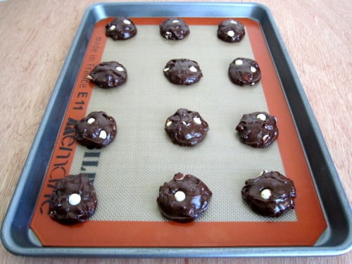 Unbaked chocolate brownie cookie dough with white chocolate chips spaced on a lined baking sheet ready for the oven.