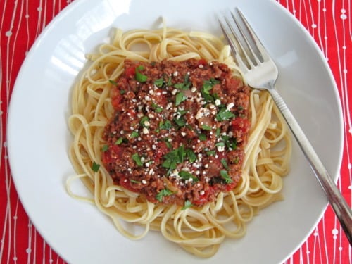 Linguine pasta topped with bolognese sauce, garnished with chopped parsley and grated cheese, served on a white plate with a fork.