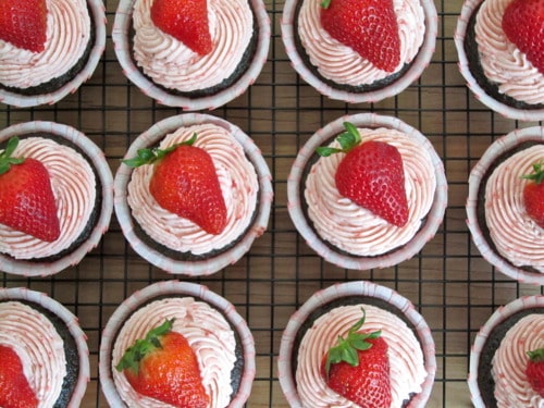 Chocolate cupcakes topped with swirled strawberry frosting and fresh halved strawberries, arranged neatly on a cooling rack.