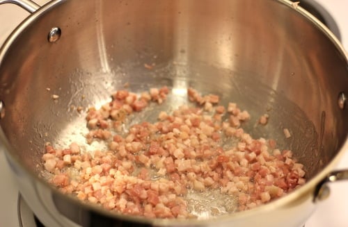 Diced pancetta sautéing in a stainless steel pot on a stovetop