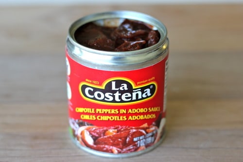 Open can of La Costeña chipotle peppers in adobo sauce on a wooden surface.