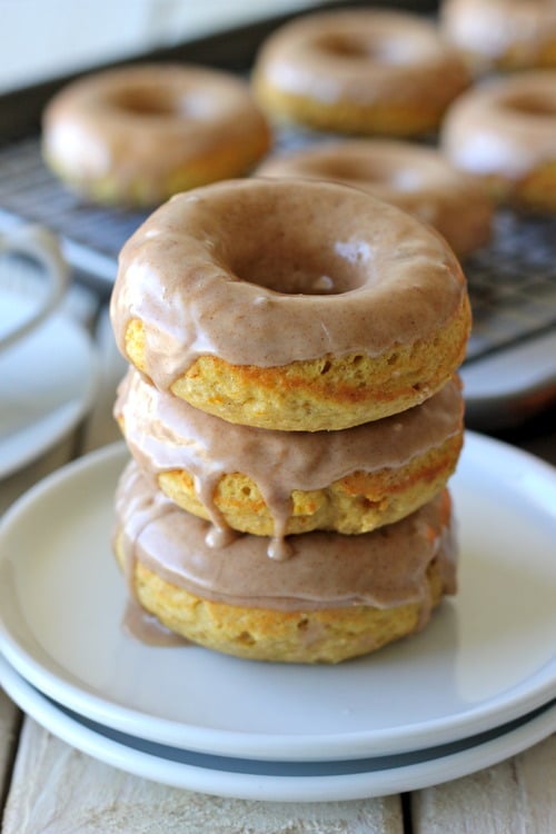 tack of baked pumpkin donuts topped with maple glaze, served on a white plate.