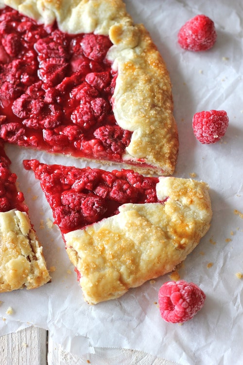 Fresh raspberry galette with golden crust sliced on parchment paper with frozen raspberries around it