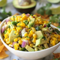Bowl of avocado corn salsa with red onion, jalapeño, and cilantro, served with tortilla chips.