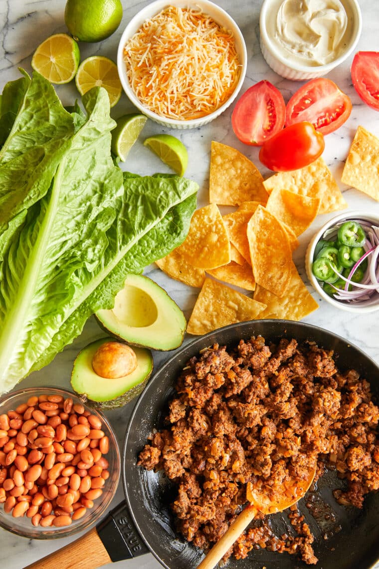 Deconstructed taco salad in a bowl with lettuce, ground beef, tomatoes, cheese, black beans, olives, tortilla chips, sour cream, and green onions.