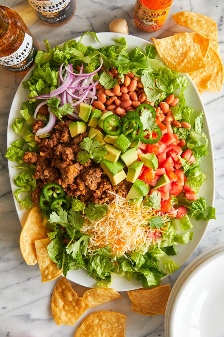 Taco salad served in a crispy tortilla bowl, filled with lettuce, ground beef, black beans, tomatoes, cheese, olives, and topped with sour cream.