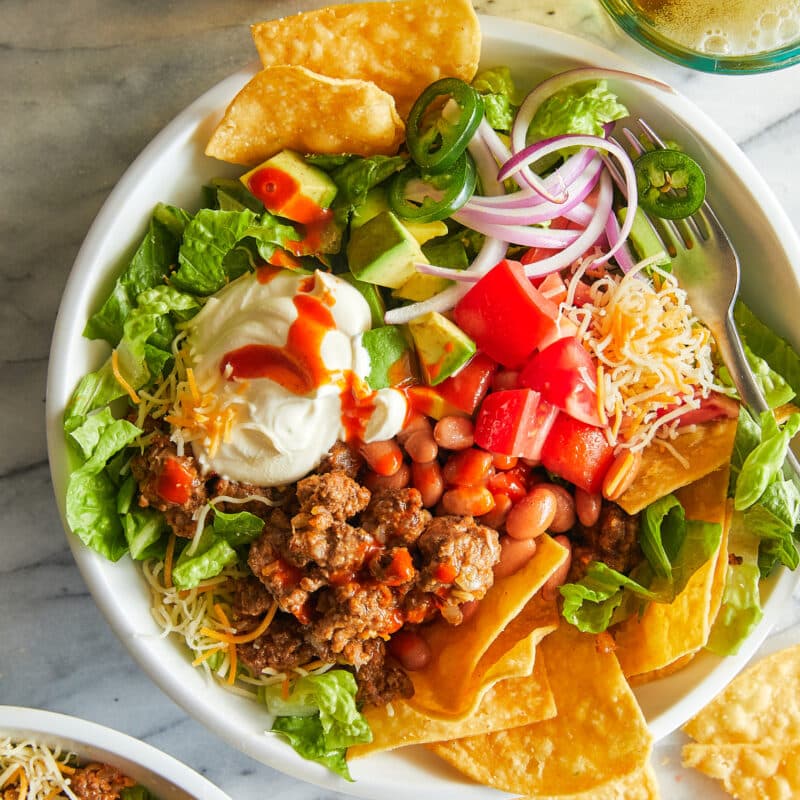 Taco salad served in a crispy tortilla bowl, filled with lettuce, ground beef, black beans, tomatoes, cheese, olives, and topped with sour cream.
