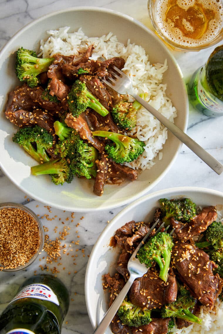Slow cooker beef and broccoli in a savory sauce served over white rice and topped with sesame seeds in a white bowl.