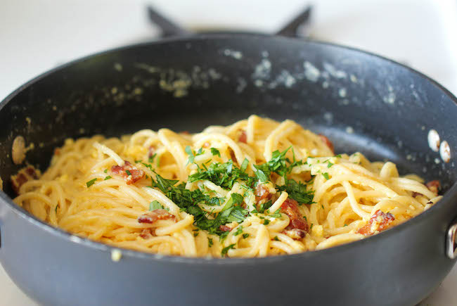 Close-up of a creamy bowl of spaghetti carbonara, topped with crispy pancetta and freshly ground black pepper, served with a fork resting on the side.