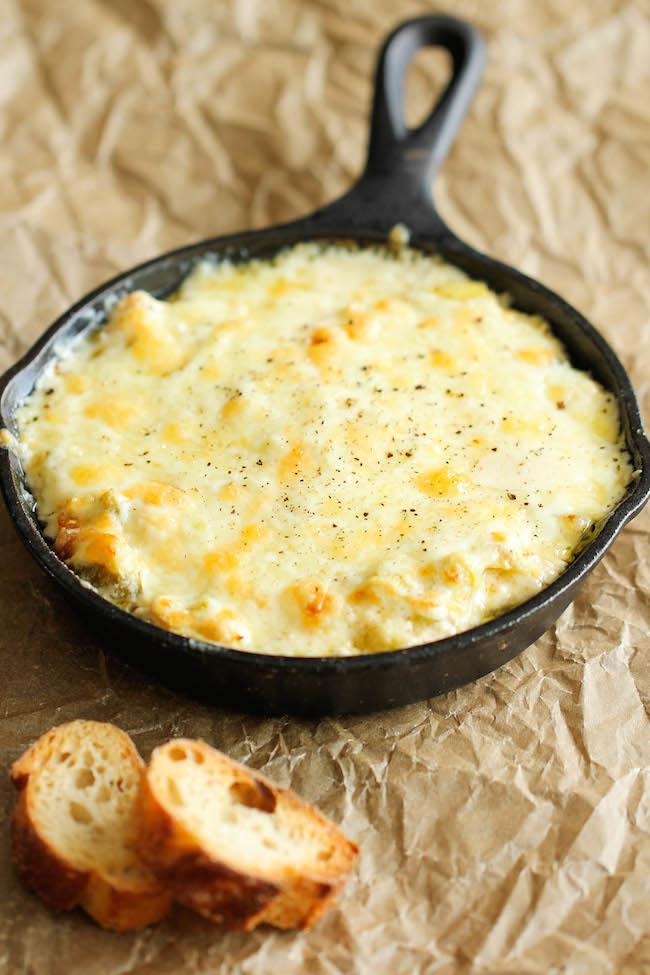 Hot crab and artichoke dip in a cast iron skillet, topped with melted cheese and served with slices of toasted baguette.