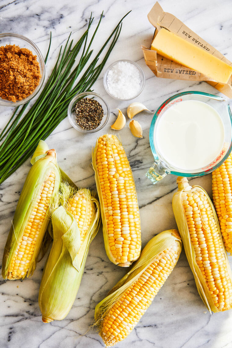 Close-up of boiled corn on the cob with melting butter and chopped herbs on top.
