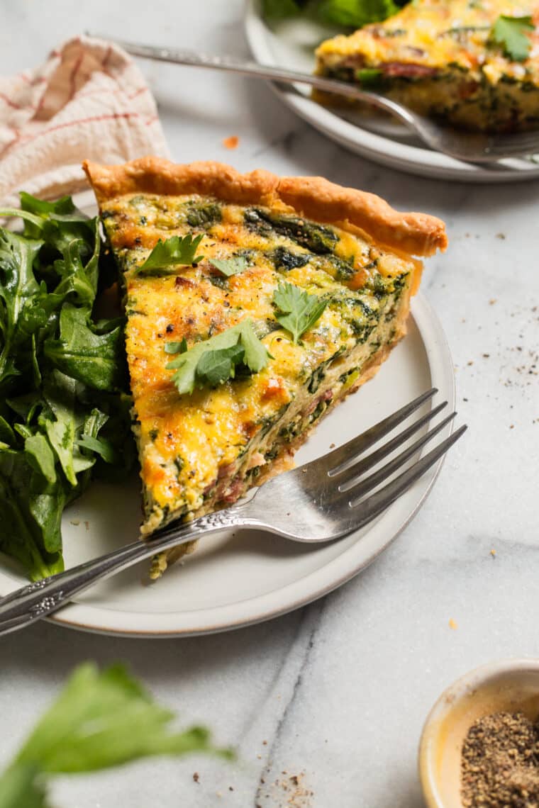 a slice of quiche on a plate with a fork and a salad